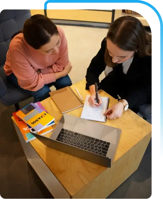 Two people are collaborating at a wooden table with a laptop, focused on SEO content writing services.